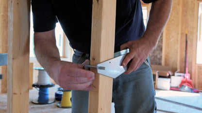 Person inserting detent pin into metal bracket on wooden stud in new construction home.