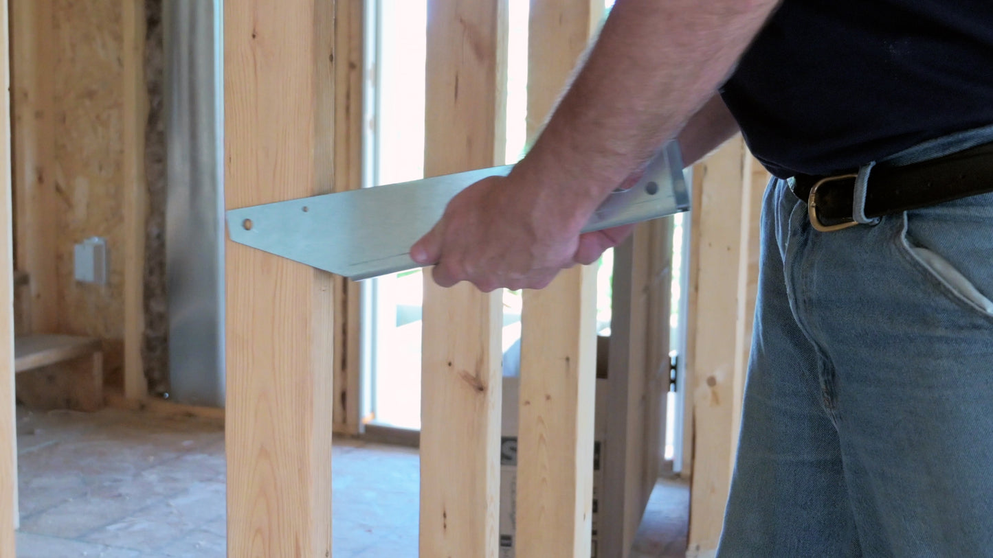 Person placing a metal bracket onto a wooden stud in new construction home.